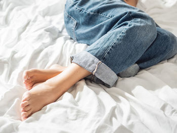 Woman in classic blue jeans on crumpled bed sheet. bedroom lit with sunlight in cozy home. 