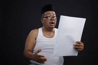 Mature man reading papers while standing against black background