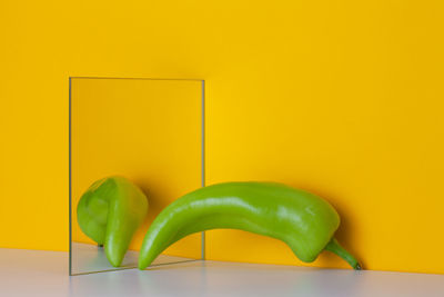 Green pepper is reflected in a mirror on a yellow background