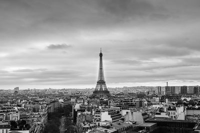 Eiffel tower amidst buildings against cloudy sky