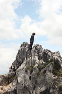 Low angle view of man standing on rock against sky