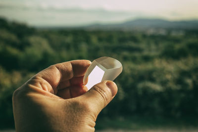 Close-up of person holding crystal against sky