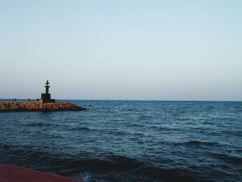 Lighthouse by calm sea against clear sky