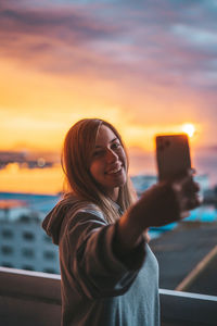 Woman taking selfie while standing against sky during sunset