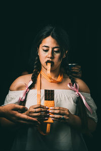 Portrait of woman holding drink against black background