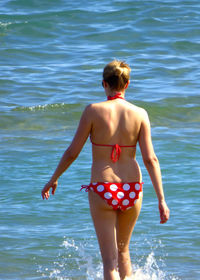 Rear view of woman in bikini walking shore at beach