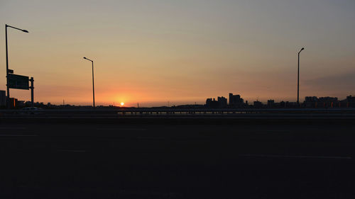 Silhouette city street against sky during sunset