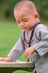 Cute boy with eyes closed standing against bench outdoors