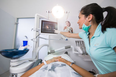 Doctor pointing at monitor with patient lying down at dentist office