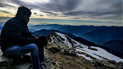 Side view of man sitting on mountain against cloudy sky