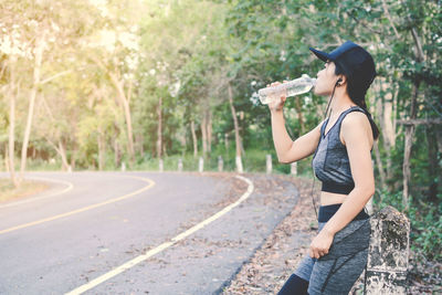 Woman drinking water by road while exercising