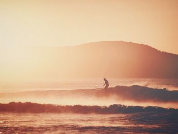 Silhouette man surfing in sea against sky during sunset