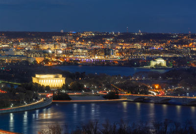 Illuminated buildings by river against sky at night