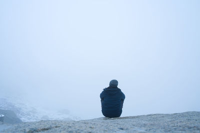 Rear view of man on rock against clear sky