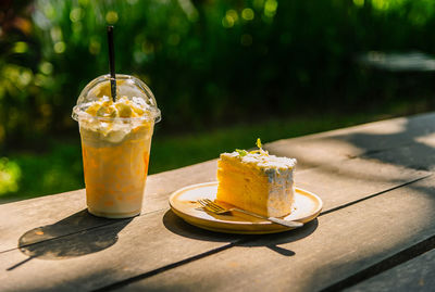 Cream coffee and a piece of cake on a white plate lay on a wood floor blurred green background.