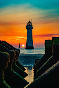 Lighthouse by sea against sky during sunset