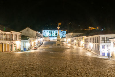 Illuminated street amidst buildings against sky at night