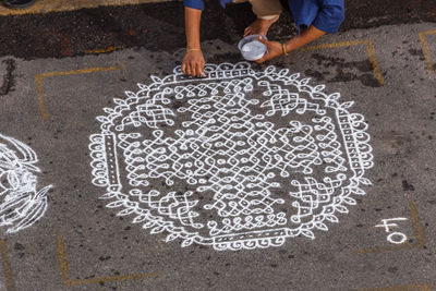 Low section of woman making rangoli on footpath during competition