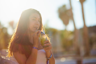 Portrait of young woman having drink during sunny day