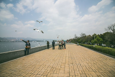 People on footpath by sea against sky