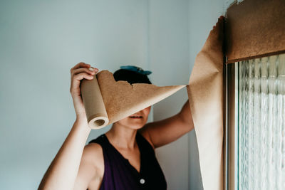 Portrait of woman holding camera while standing against wall at home