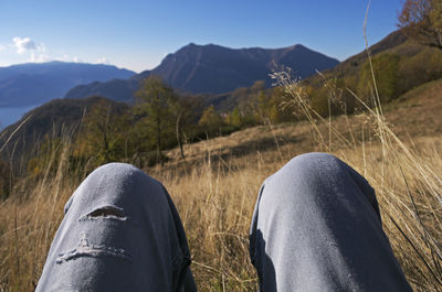 Cropped image of person relaxing on grassy field against mountains