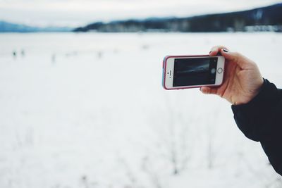 Close-up of hand photographing with mobile phone on snow