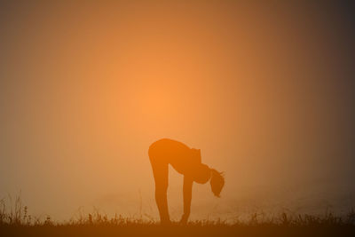 Silhouette woman practicing yoga on field against sky during sunset