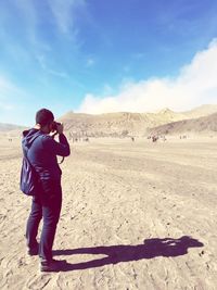 Full length of man photographing at desert against sky during sunny day