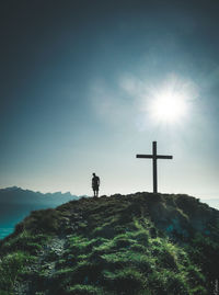 Silhouette person standing on cross on mountain against sky
