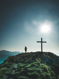 Silhouette person standing on cross on mountain against sky