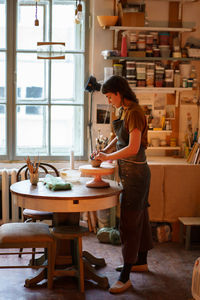 Young female potter maker work with clay on pottery wheel in creative space or professional studio