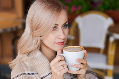 Portrait pretty blonde woman, smiling woman in cozy plaid, sitting in cafe