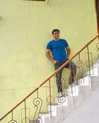 Portrait of young man standing on staircase against wall