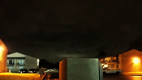 Illuminated street light by building against sky at night