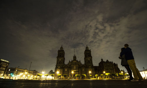 Man and woman standing against metropolitan cathedral in city at night