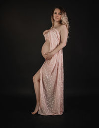 Portrait of young woman standing against black background