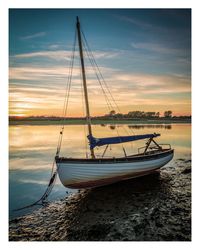 Sailboats moored in sea against sky during sunset