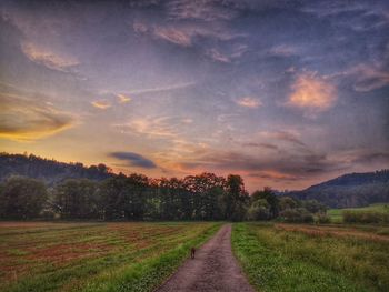 Empty road amidst field against sky during sunset