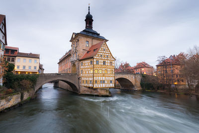 Arch bridge over river amidst buildings against sky