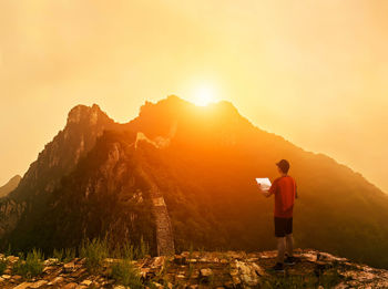 Man reading map while standing against mountains during sunset