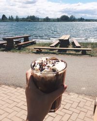 Close-up of hand holding ice cream by lake against sky