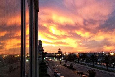 Road by cityscape against sky during sunset