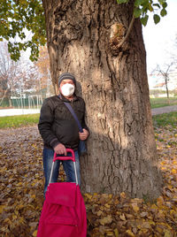Man holding umbrella standing by tree trunk
