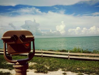 Coin-operated binoculars by sea against cloudy sky