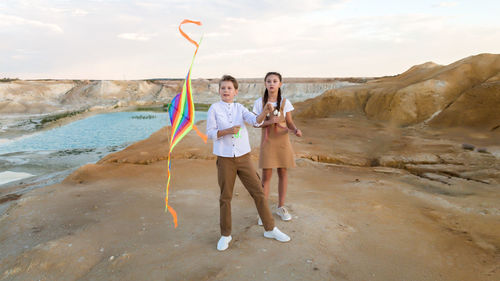 A girl watches as boy deftly launches a kite into the sky.