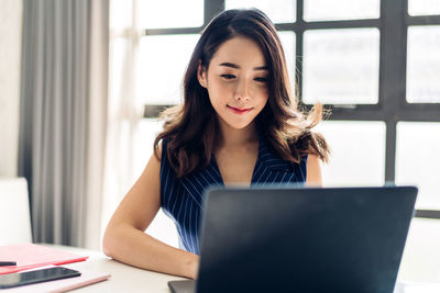 Young woman using phone while sitting on table