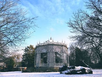 Bare trees on snow covered building against sky