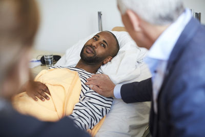 Young man looking at family while lying on bed at hospital