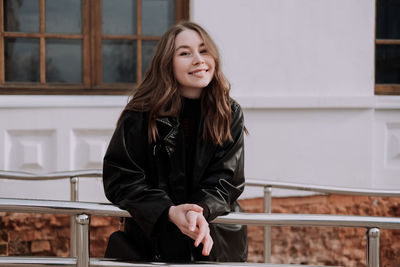 Portrait of smiling young woman standing against railing